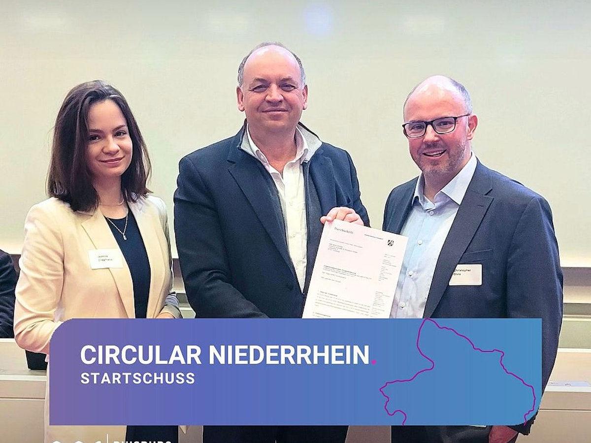 Drei Personen in Geschäftskleidung stehen nebeneinander und lächeln in die Kamera. Der Mann in der Mitte hält ein Dokument in der Hand. Auf einem Banner am unteren Bildrand steht: „Circular Niederrhein Startschuss“ mit dem Logo von „Duisburg Business & Innovation“.