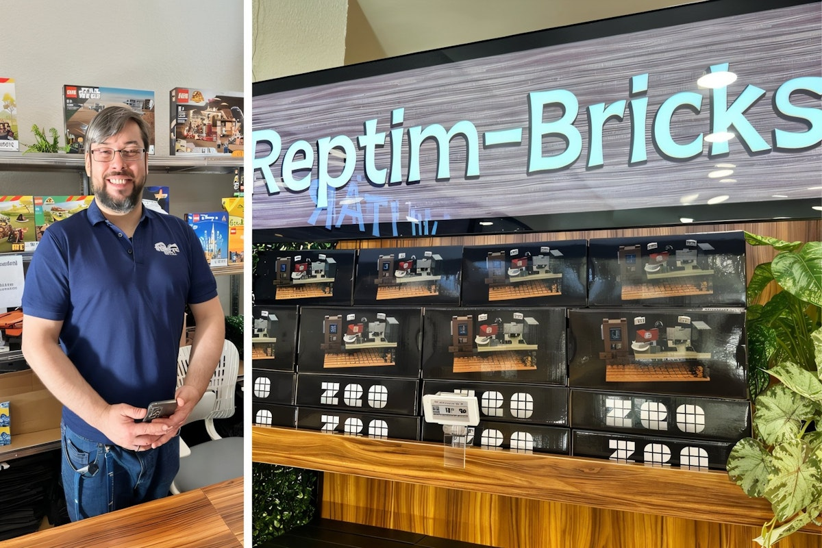 Ein lächelnder Mann steht in einem Spielzeugladen neben Regalen mit LEGO-Sets. Auf der angrenzenden Ausstellungsfläche sind verpackte Spielzeugsets unter einem großen „Reptim-Bricks“-Schild ausgestellt, an deren Seite grüne Pflanzen zu sehen sind.