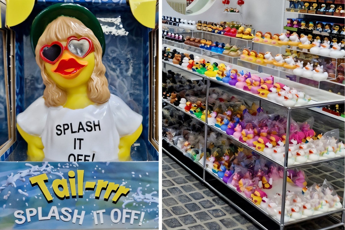 In einem Geschäft steht eine Schaufensterpuppe mit einer Herzbrille und einem „SPLASH IT OFF!“-T-Shirt neben Regalen, die mit verschiedenen bunten Gummienten gefüllt sind.